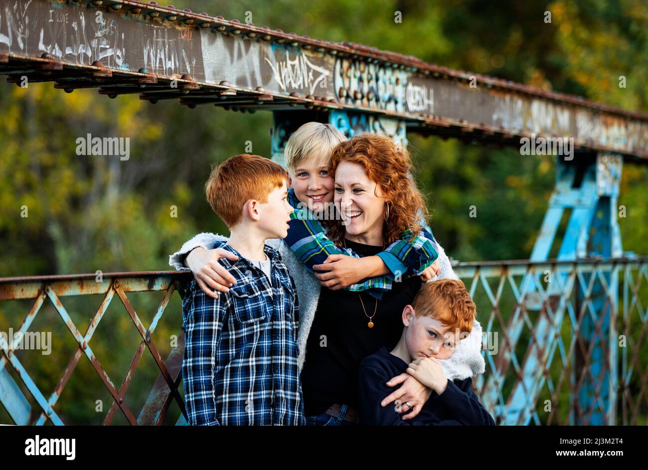 Mutter mit drei Jungen, die im Herbst auf einer Brücke in einem Park stehen; Edmonton, Alberta, Kanada Stockfoto
