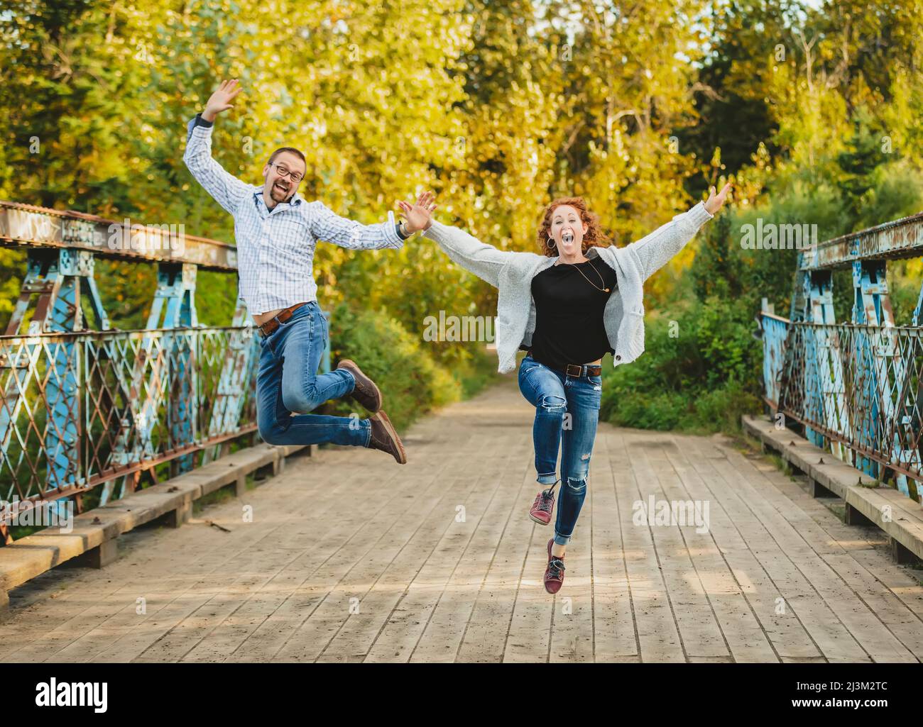 Reifes Ehepaar draußen in einem Park springt mitten in der Luft in ausgelassenen Feier; Edmonton, Alberta, Kanada Stockfoto