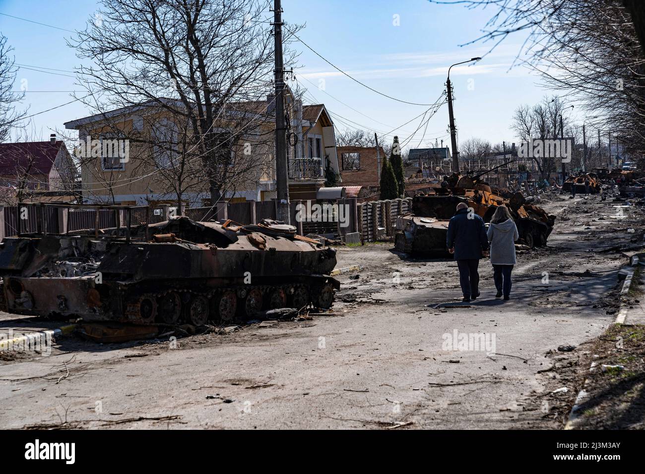 Ein Mann und eine Frau gehen nach der Befreiung der Stadt von russischen Eindringlingen auf einer Straße, die mit zerstörten Militärfahrzeugen gesäumt ist, Bucha, Region Kiew, Nordukraine, April 7, 2022. Nach Angaben des Bürgermeisters wurden nach einem Massenmord in Bucha mehr als 300 Einwohner der Stadt tot aufgefunden. Die Ukraine hat den Internationalen Strafgerichtshof gebeten, im Rahmen der laufenden Untersuchung der Invasion zu untersuchen, was in der Stadt geschehen ist, um festzustellen, ob eine Reihe russischer Kriegsverbrechen begangen wurden.[die russischen Behörden haben die Verantwortung verweigert und behauptet, dass die Ukraine Aufnahmen des E gefälscht habe Stockfoto