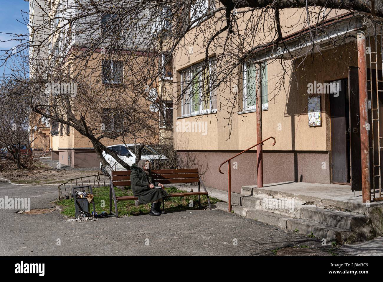 Nach der Befreiung der Stadt von den russischen Eindringlingen in Bucha, Region Kiew, Nordukraine, im April 7, sonnt sich eine ältere Frau auf einer Bank vor einem Wohngebäude in der Sonne. 2022. Nach Angaben des Bürgermeisters wurden nach einem Massenmord in Bucha mehr als 300 Einwohner der Stadt tot aufgefunden. Die Ukraine hat den Internationalen Strafgerichtshof gebeten, im Rahmen der laufenden Untersuchung der Invasion zu untersuchen, was in der Stadt geschehen ist, um festzustellen, ob eine Reihe russischer Kriegsverbrechen begangen wurden.[die russischen Behörden haben die Verantwortung verweigert und behauptet, dass die Ukraine Aufnahmen des Militärs gefälscht habe Stockfoto
