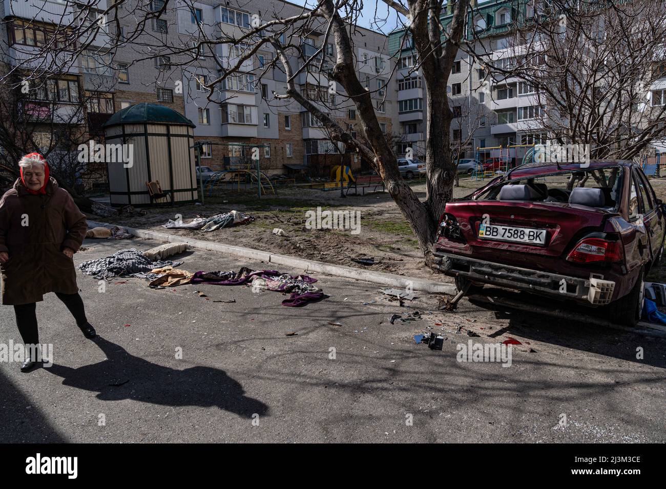 Eine ältere Frau bleibt nach der Befreiung der Stadt von russischen Eindringlingen in Bucha, Region Kiew, Nordukraine, am 7. April auf einer Straße in der Nähe eines beschädigten Autos. 2022. Nach Angaben des Bürgermeisters wurden nach einem Massenmord in Bucha mehr als 300 Einwohner der Stadt tot aufgefunden. Die Ukraine hat den IStGH gebeten, zu untersuchen, was in der Stadt im Rahmen ihrer laufenden Untersuchung der Invasion geschehen ist, um festzustellen, ob eine Reihe von russischen Kriegsverbrechen begangen wurden.[die russischen Behörden haben die Verantwortung verweigert und behauptet, dass die Ukraine Aufnahmen des Ereignisses gefälscht oder inszeniert hat Töten Stockfoto