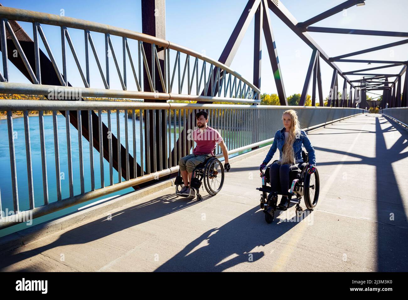 Junge querschnittsgelähmte Männer und Frauen, die an einem schönen Herbsttag gemeinsam mit ihren Rollstühlen über eine Brücke gehen; Edmonton, Alberta, Kanada Stockfoto
