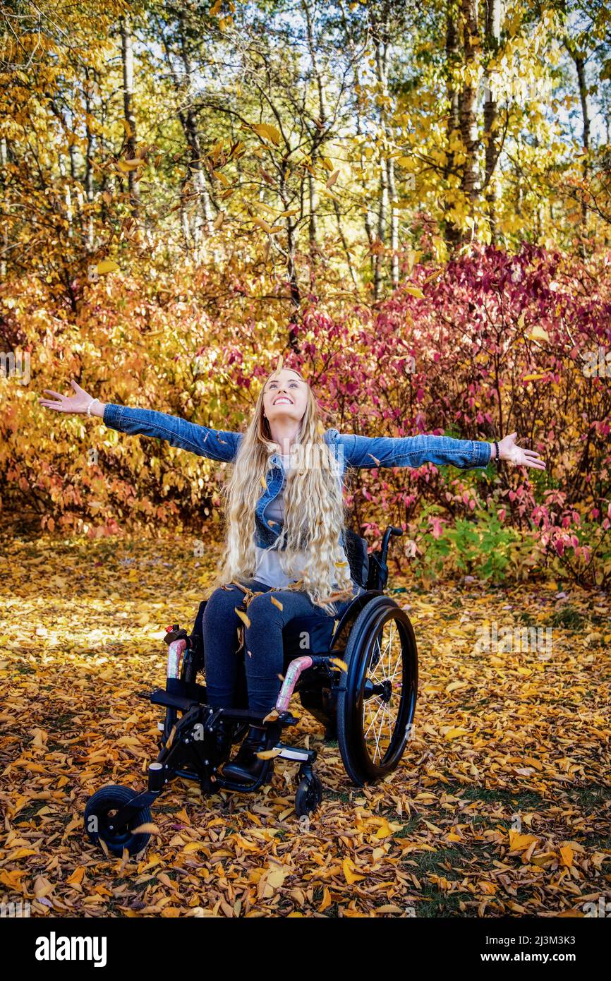 Eine junge querschnittsgelähmte Frau in ihrem Rollstuhl an einem schönen Herbsttag in einem Park, die Arme überflügelt und die Natur genossen; Edmonton, Alberta, Kanada Stockfoto