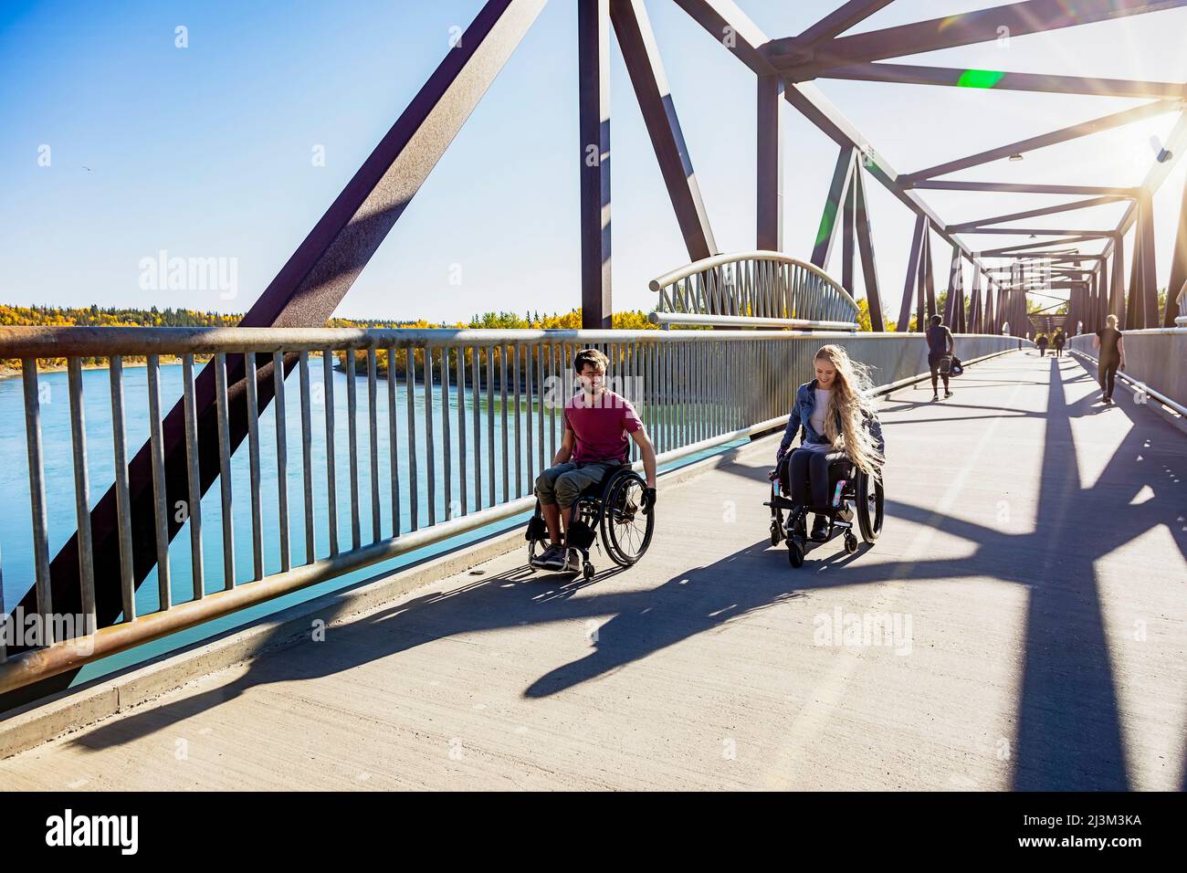 Junge querschnittsgelähmte Männer und Frauen, die an einem schönen Herbsttag gemeinsam mit ihren Rollstühlen über eine Brücke gehen; Edmonton, Alberta, Kanada Stockfoto