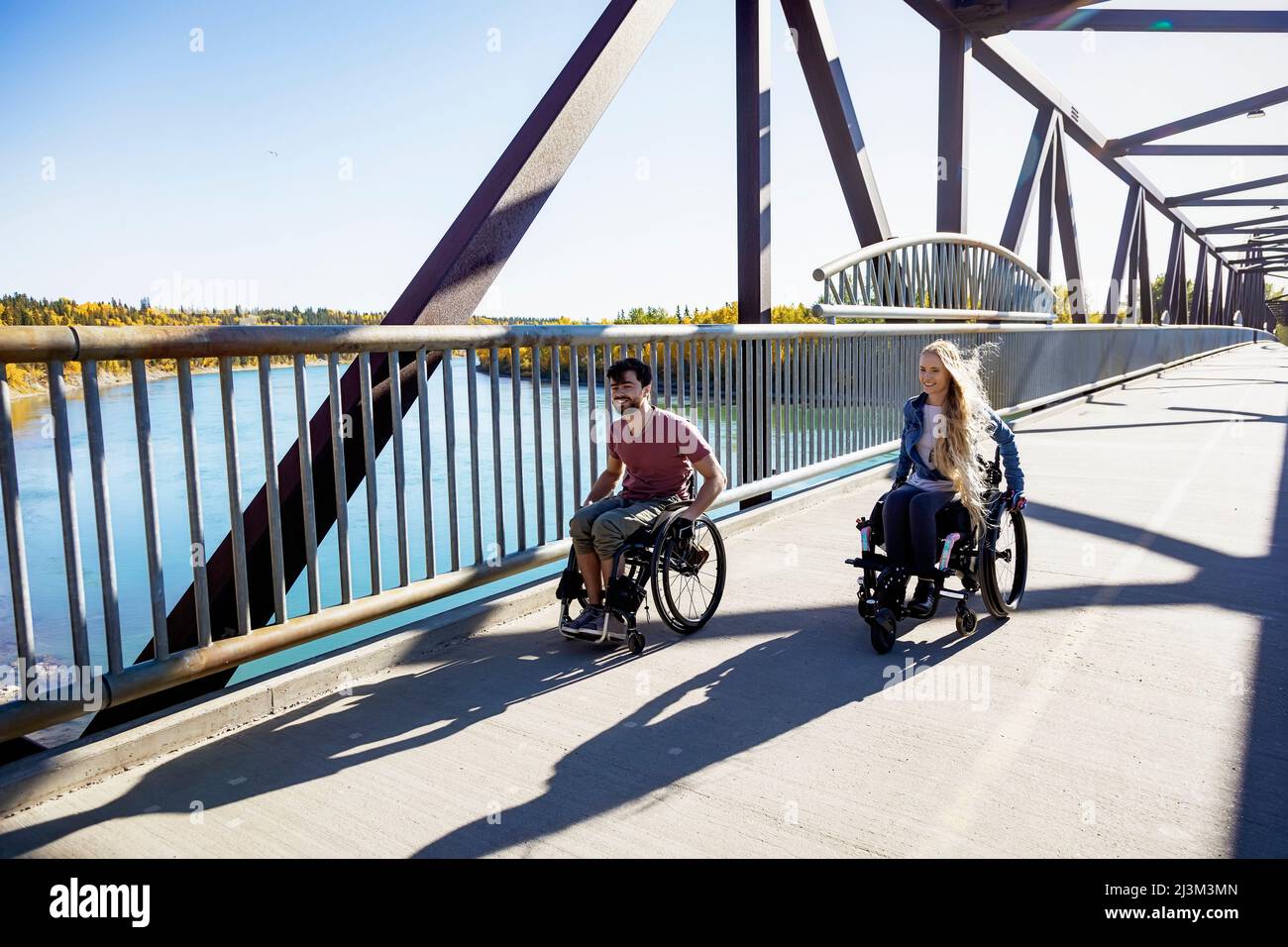 Junge querschnittsgelähmte Männer und Frauen, die an einem schönen Herbsttag gemeinsam mit ihren Rollstühlen über eine Brücke gehen; Edmonton, Alberta, Kanada Stockfoto