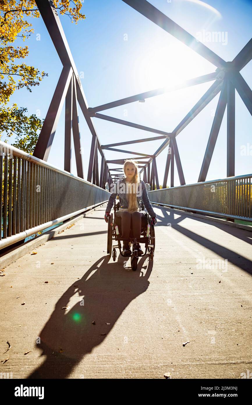 Eine junge querschnittsgelähmte Frau, die an einem schönen Herbsttag mit ihrem Rollstuhl über eine Brücke geht; Edmonton, Alberta, Kanada Stockfoto