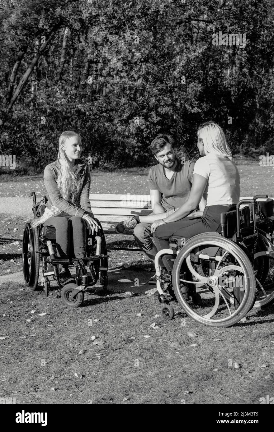 Schwarz-Weiß-Bild einer Gruppe von drei jungen Querschnittsgelähmten in ihren Rollstühlen, die an einem schönen sonnigen Tag gemeinsam in einem Park zu Besuch sind Stockfoto