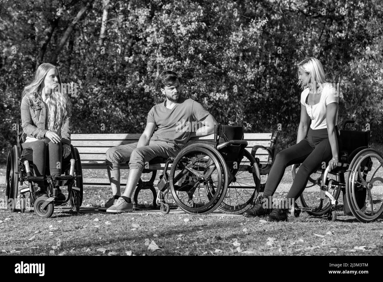 Schwarz-Weiß-Bild einer Gruppe von drei jungen Querschnittsgelähmten in ihren Rollstühlen, die an einem schönen sonnigen Tag gemeinsam in einem Park zu Besuch sind Stockfoto