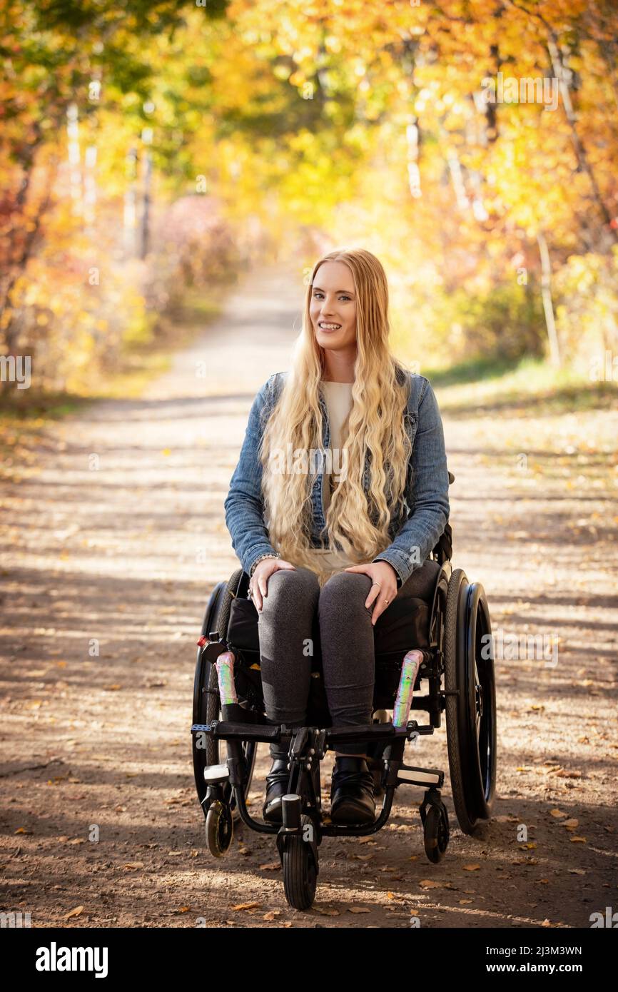 Eine junge querschnittsgelähmte Frau im Rollstuhl, die an einem schönen Herbsttag in einem Park eine Spur zurücklegt; Edmonton, Alberta, Kanada Stockfoto