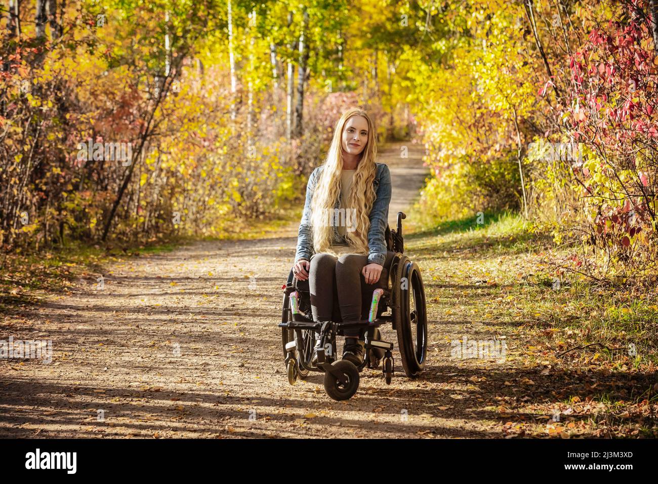 Eine junge querschnittsgelähmte Frau im Rollstuhl, die an einem schönen Herbsttag in einem Park eine Spur zurücklegt; Edmonton, Alberta, Kanada Stockfoto