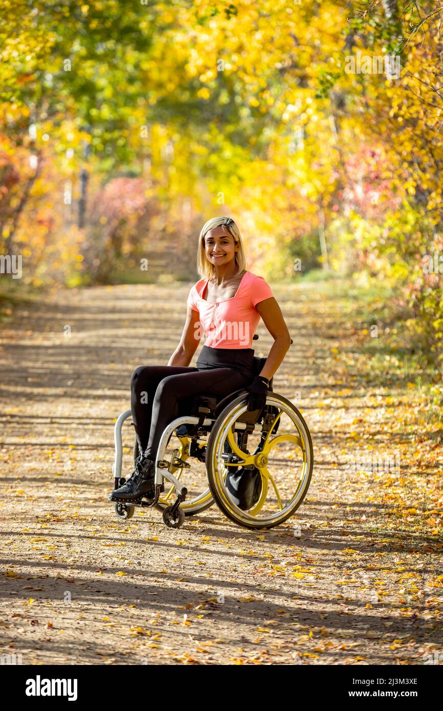 Porträt einer jungen querschnittsgelähmten Frau in ihrem Rollstuhl auf einem Pfad in einem Park an einem schönen Herbsttag; Edmonton, Alberta, Kanada Stockfoto