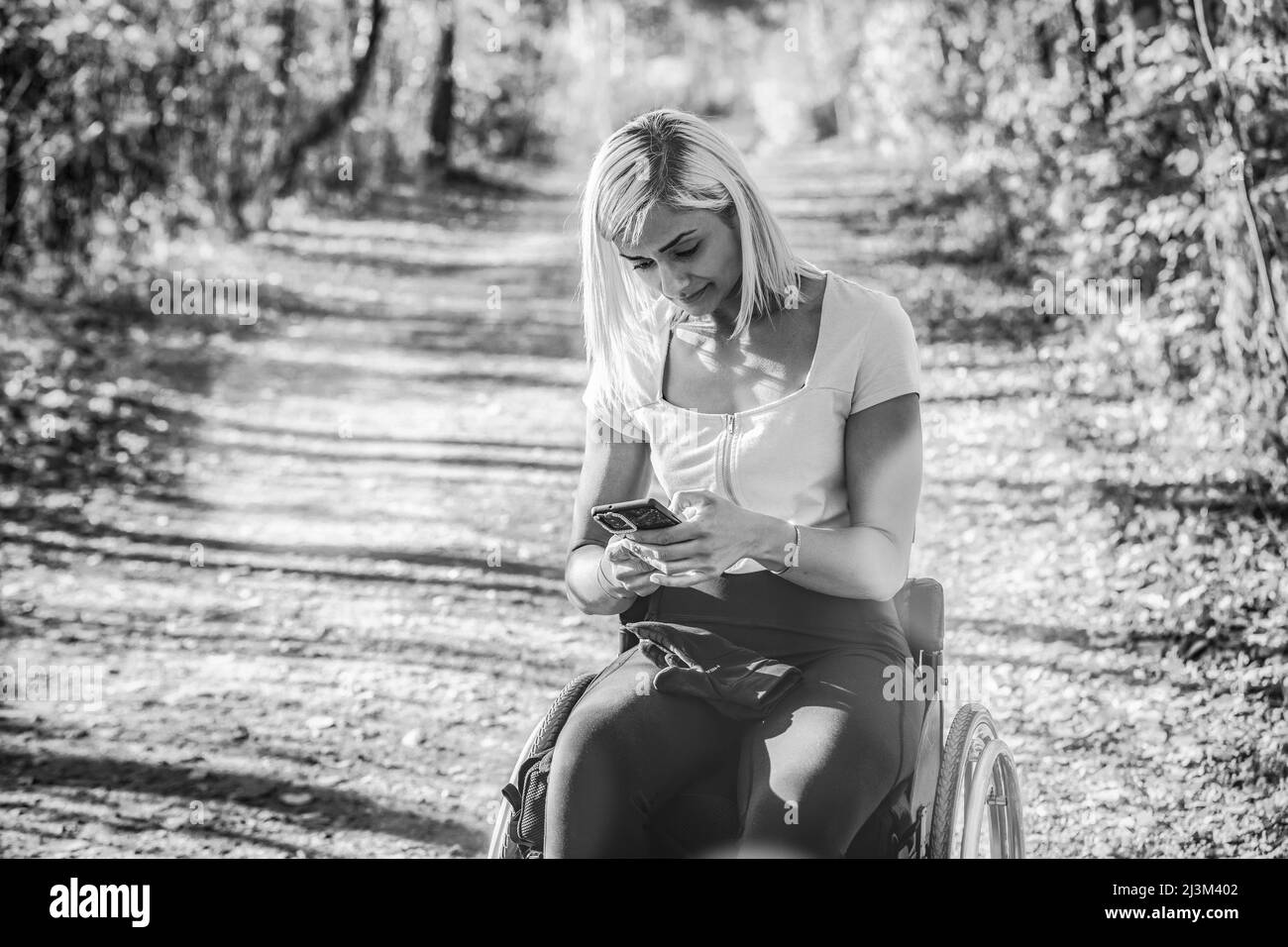 Junge querschnittsgelähmte Frau im Rollstuhl, die mit ihrem Smartphone in einem Park unterwegs ist; Edmonton, Alberta, Kanada Stockfoto