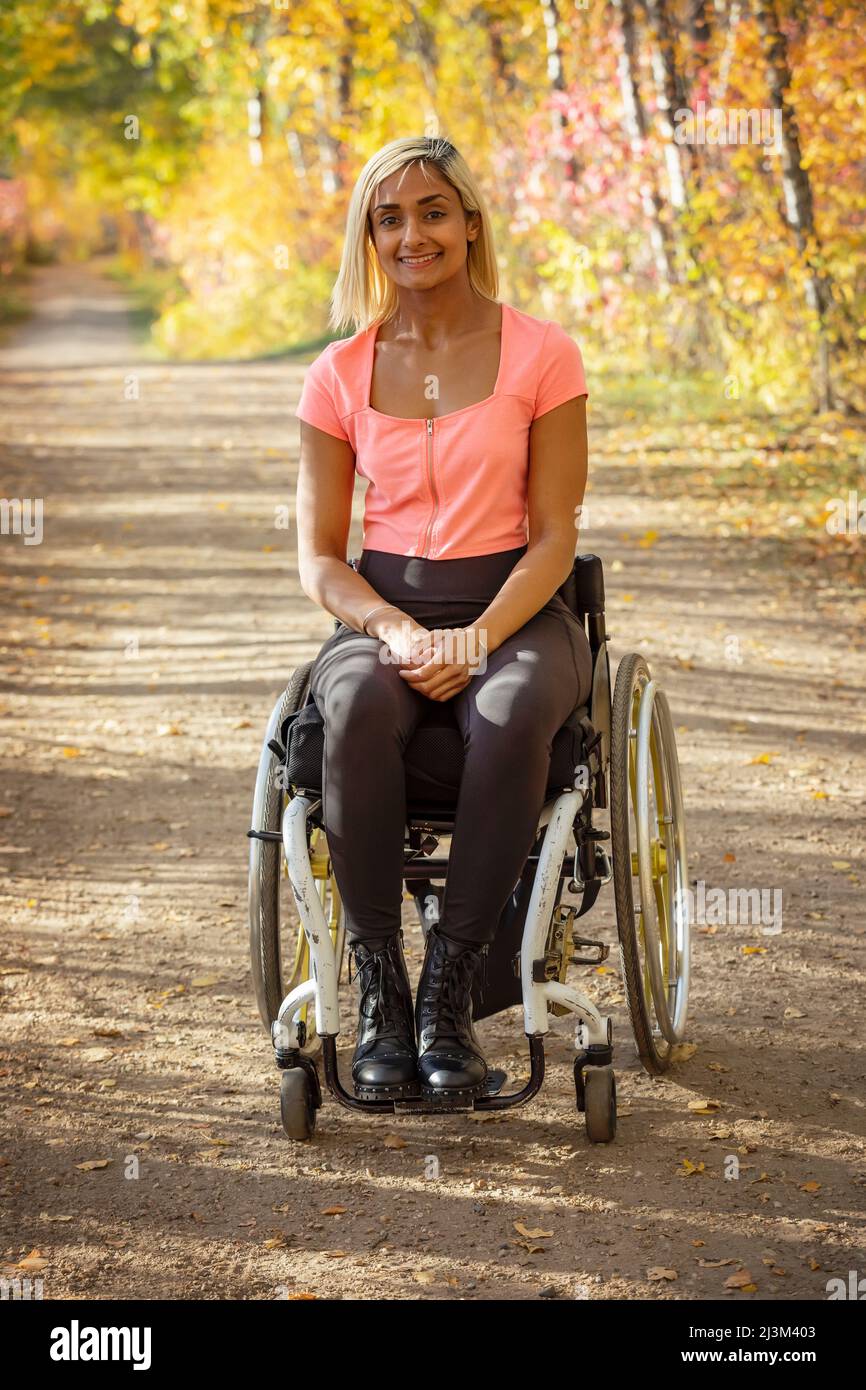 Porträt einer jungen querschnittsgelähmten Frau in ihrem Rollstuhl auf einem Pfad in einem Park an einem schönen Herbsttag; Edmonton, Alberta, Kanada Stockfoto