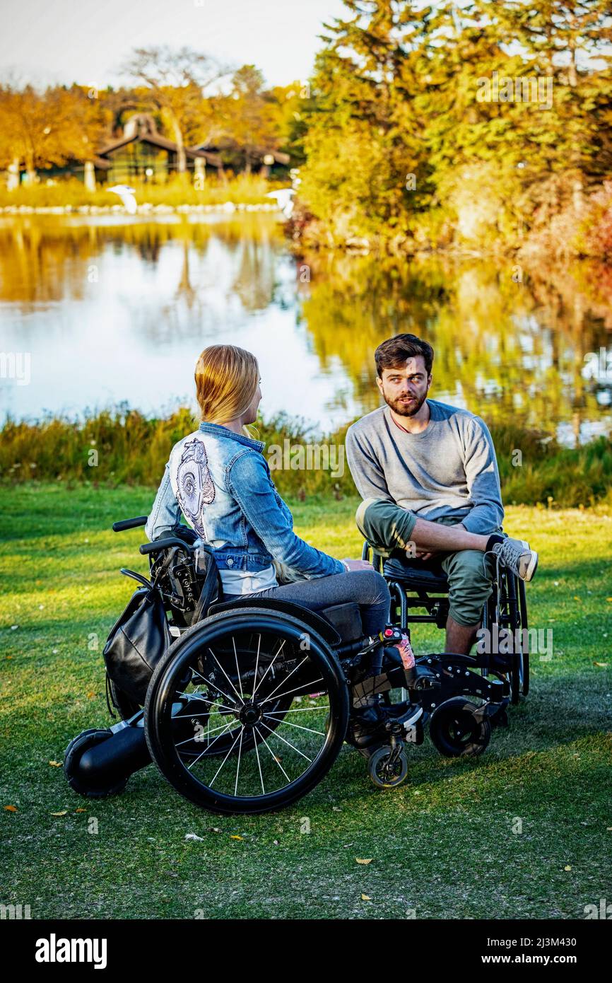 Junge Querschnittsgelähmte im Rollstuhl besuchen gemeinsam an einem schönen Herbsttag einen Park; Edmonton, Alberta, Kanada Stockfoto