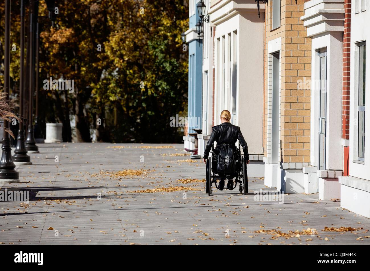 Eine junge querschnittsgelähmte Frau im Rollstuhl, die an einem schönen Herbsttag einen Stadtpfad entlang geht; Edmonton, Alberta, Kanada Stockfoto