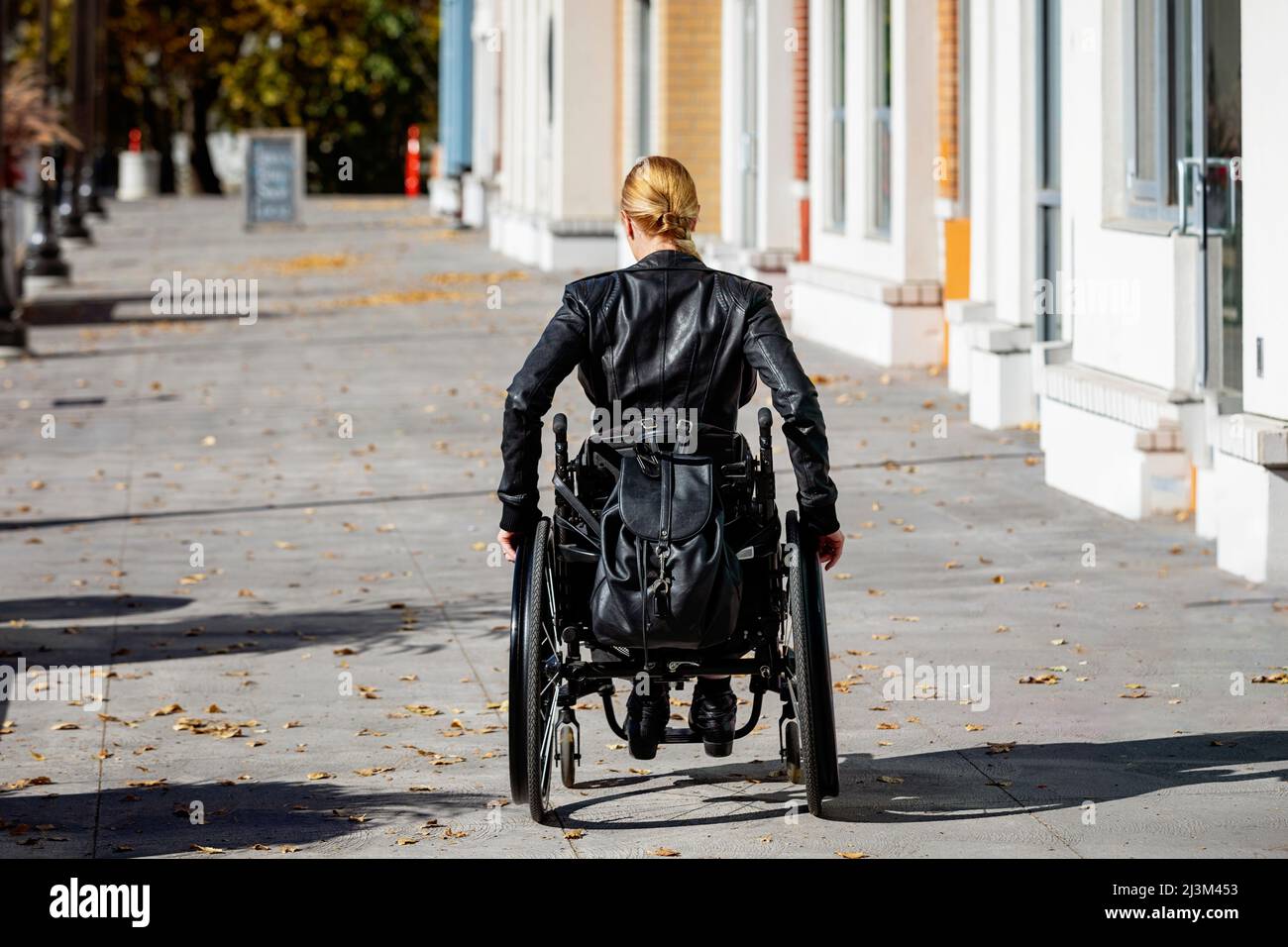 Eine junge querschnittsgelähmte Frau im Rollstuhl, die an einem schönen Herbsttag einen Stadtpfad entlang geht; Edmonton, Alberta, Kanada Stockfoto