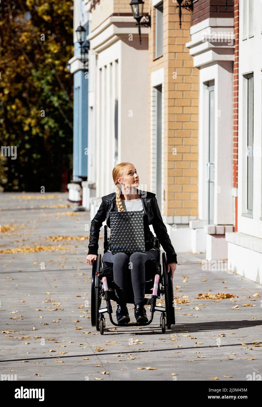 Eine junge querschnittsgelähmte Frau in ihrem Rollstuhl mit einer Einkaufstasche, die an einem schönen Herbsttag einen Stadtgang entlang geht; Edmonton, Alberta, Kanada Stockfoto