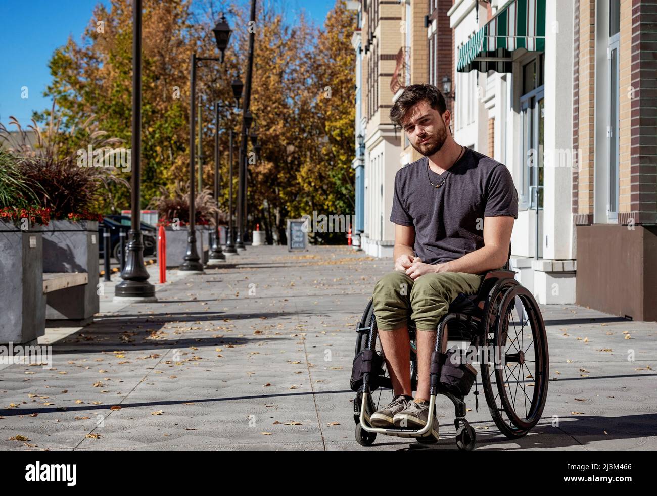 Außenportrait eines jungen querschnittsgelähmten Mannes in seinem Rollstuhl auf einem Bürgersteig an einem schönen Herbsttag; Edmonton, Alberta, Kanada Stockfoto