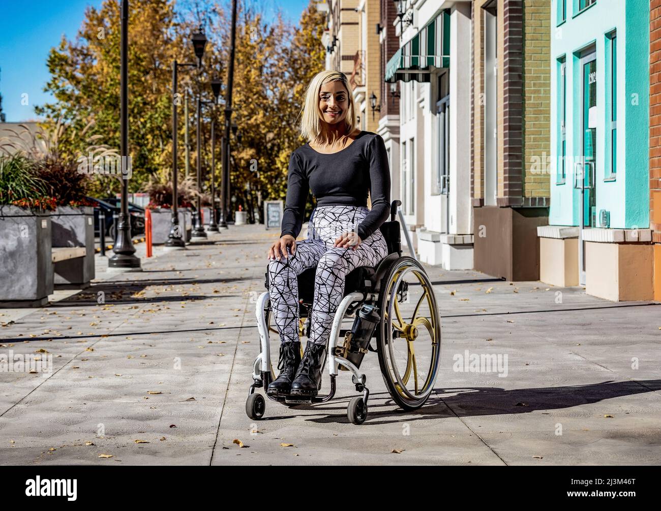 Außenportrait einer jungen querschnittsgelähmten Frau in ihrem Rollstuhl auf einem Bürgersteig an einem schönen Herbsttag; Edmonton, Alberta, Kanada Stockfoto