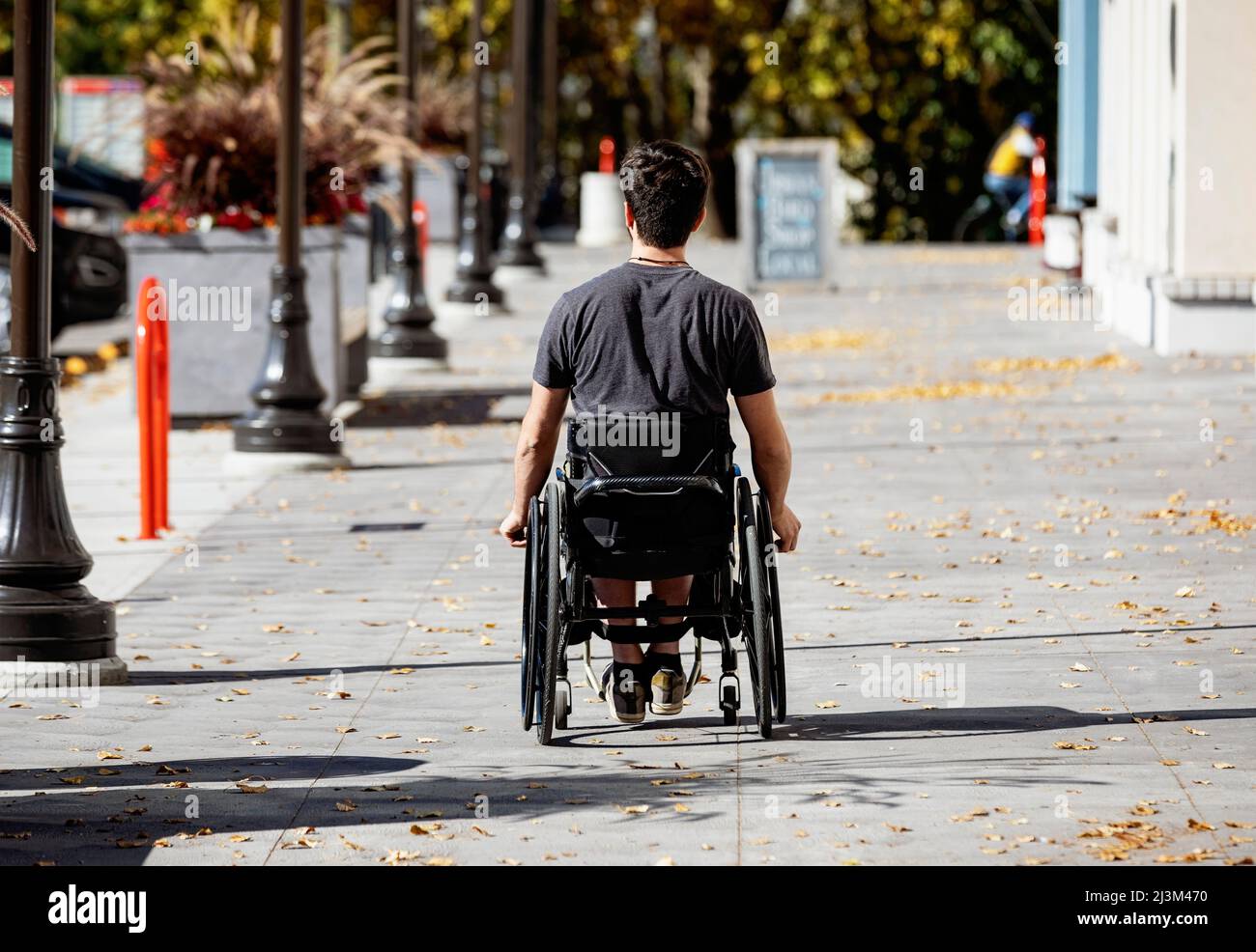 Ein junger Querschnittsgelähmter im Rollstuhl, der an einem schönen Herbsttag einen Stadtpfad entlang geht; Edmonton, Alberta, Kanada Stockfoto