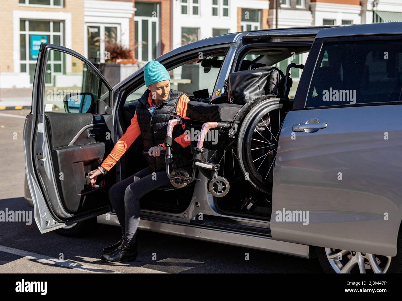 Die junge querschnittsgelähmte Frau bewegt sich von ihrem Rollstuhl auf den Fahrersitz eines Autos und lädt den Rollstuhl in einem angepassten Fahrzeug auf den Rücksitz Stockfoto