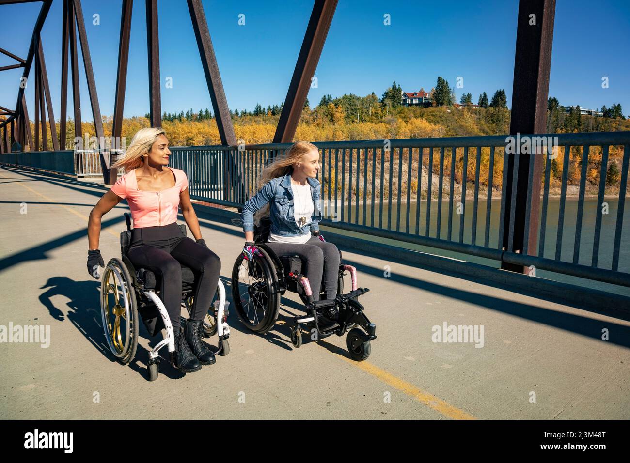 Zwei junge querschnittsgelähmte Frauen in ihren Rollstühlen, die an einem schönen Herbsttag in einem Park sitzen; Edmonton, Alberta, Kanada Stockfoto