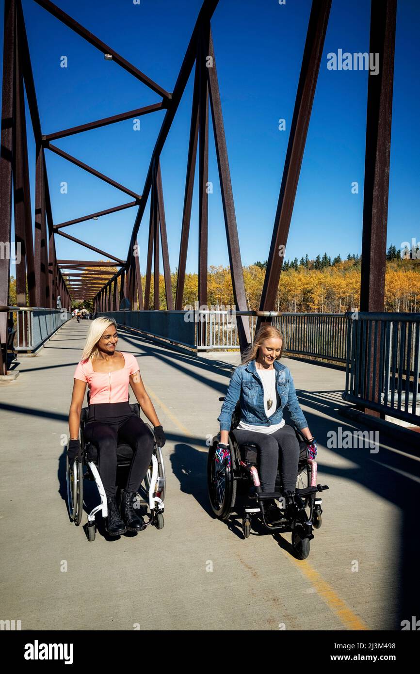 Zwei junge querschnittsgelähmte Frauen in ihren Rollstühlen, die an einem schönen Herbsttag in einem Park sitzen; Edmonton, Alberta, Kanada Stockfoto