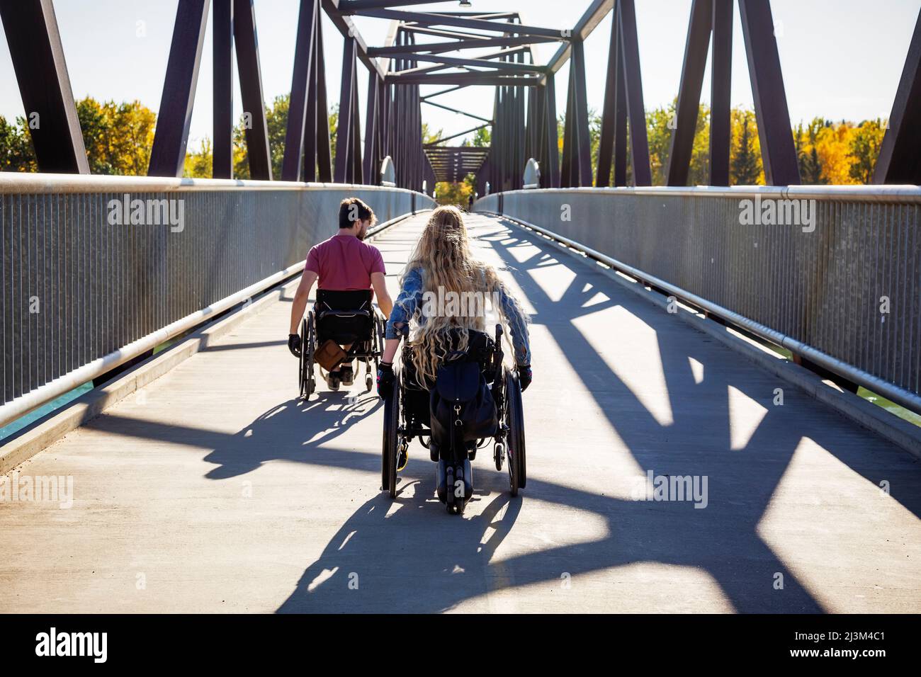 Junge querschnittsgelähmte Männer und Frauen, die an einem schönen Herbsttag gemeinsam mit ihren Rollstühlen über eine Brücke gehen; Edmonton, Alberta, Kanada Stockfoto