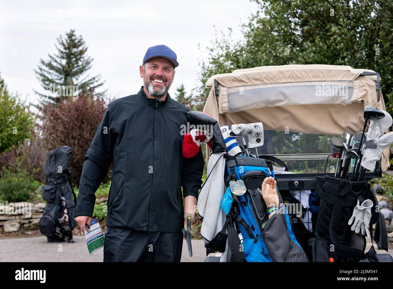 Golfer mit Armprothese, der neben einem Golfwagen auf einem Golfplatz steht; Okotoks, Alberta, Kanada Stockfoto