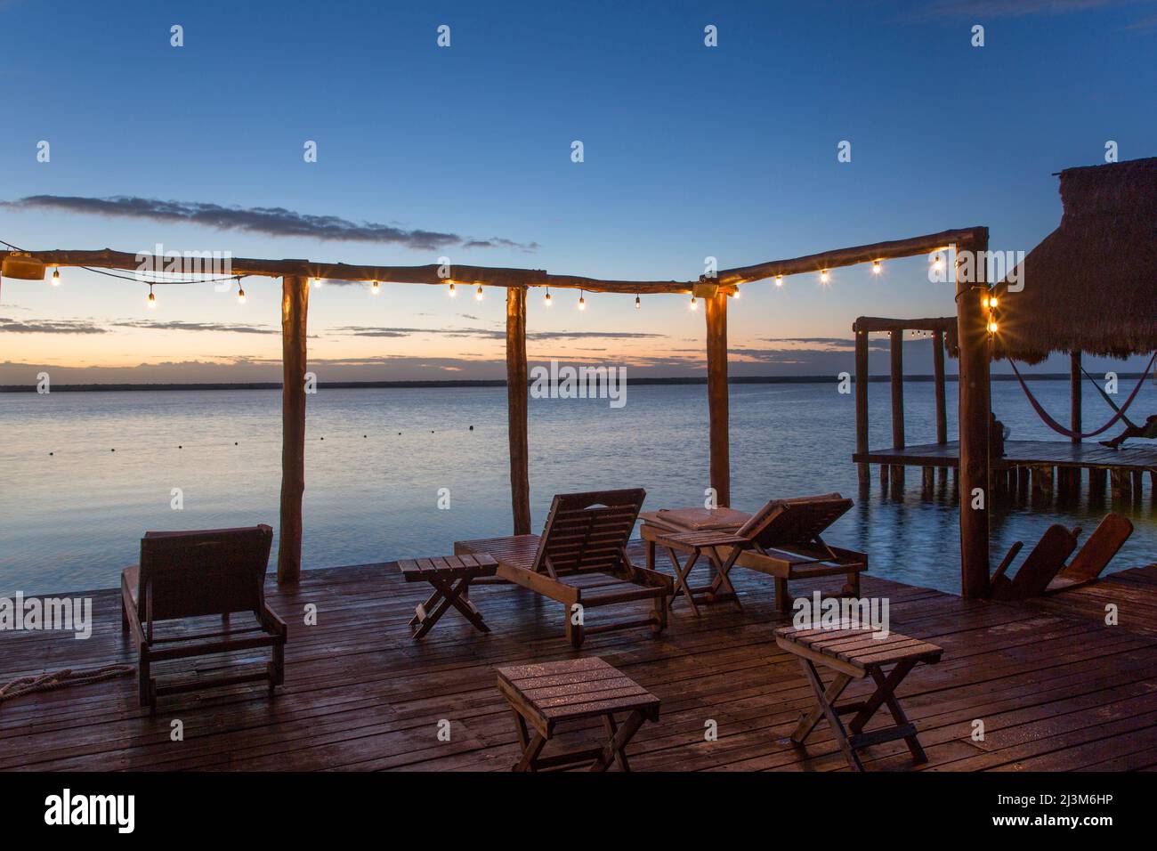 Dock mit Sitzgelegenheiten und einer Reihe von beleuchteten Lichtern am Wasser im Rancho Encantado Eco-Resort & Spa; Bacalar, Quintana Roo, Mexiko Stockfoto