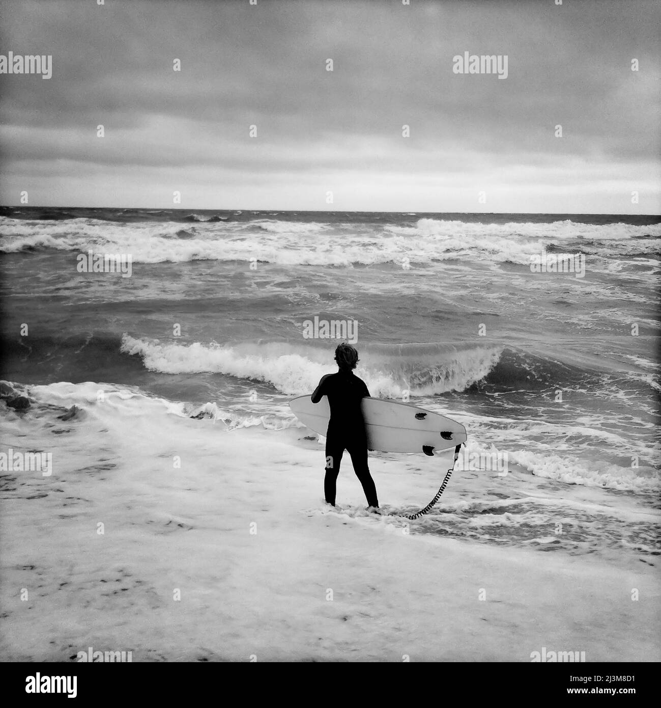 Ein 12-jähriger Junge starrt auf unordentliche Brandung und wartet auf seine Chance, auf seinem Surfbrett zu steigen.; Nags Head, North Carolina. Stockfoto
