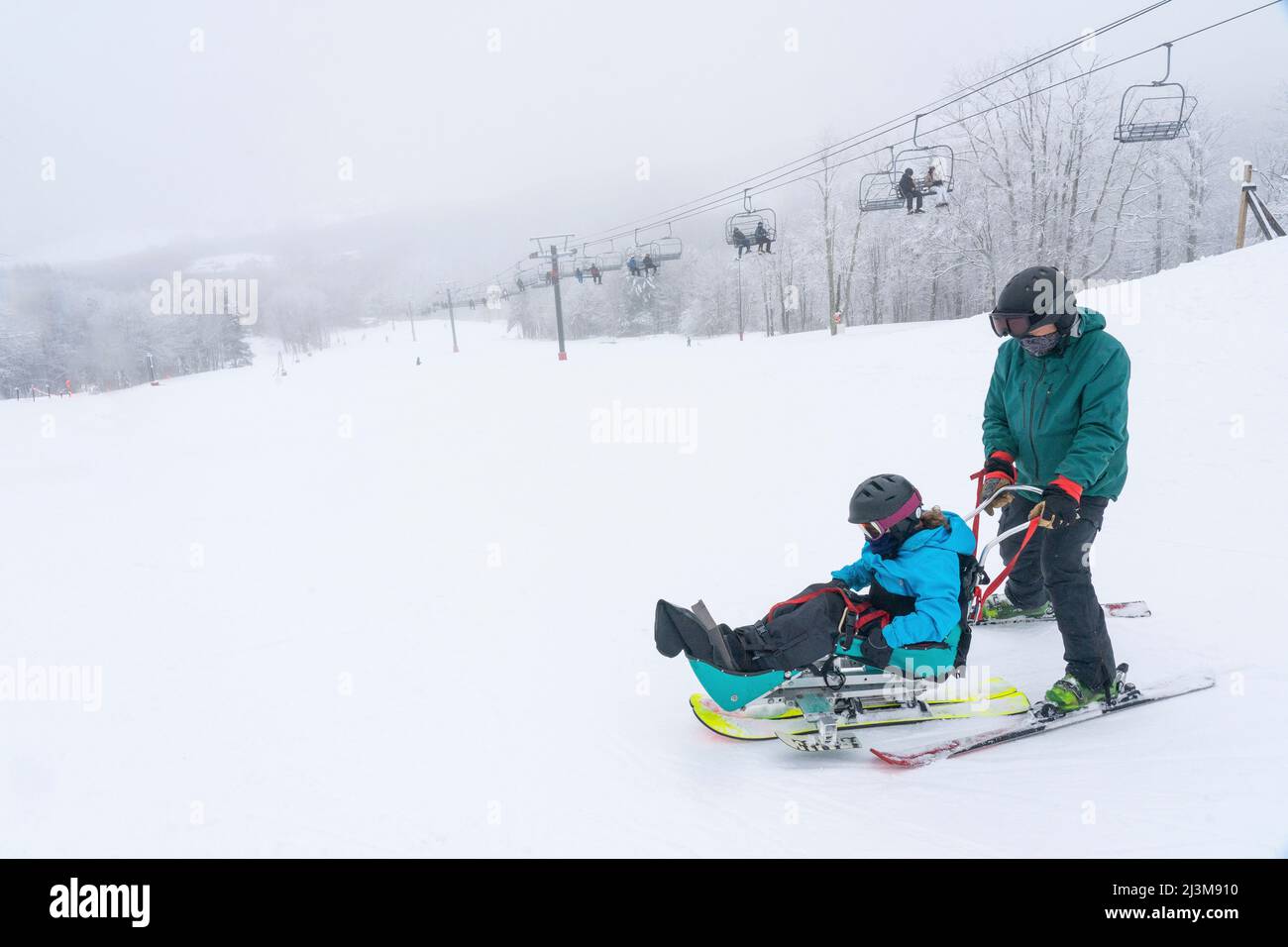 Adaptives Skifahren für ein Mädchen mit Ullrich kongenitaler Muskeldystrophie, in einem Skigebiet mit einem Instruktor Stockfoto