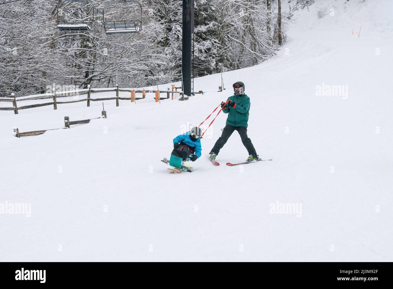 Adaptives Skifahren für ein Mädchen mit Ullrich kongenitaler Muskeldystrophie, in einem Skigebiet mit einem Instruktor Stockfoto