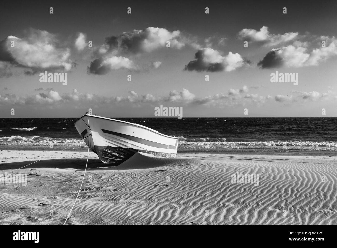Einsames Holzboot am Strand in der Nähe von Dünen in Bolonia, Andalusien, Spanien. Diese Düne ist über 30 Meter hoch und 200 Meter breit.Schwarz-Weiß-Phot Stockfoto