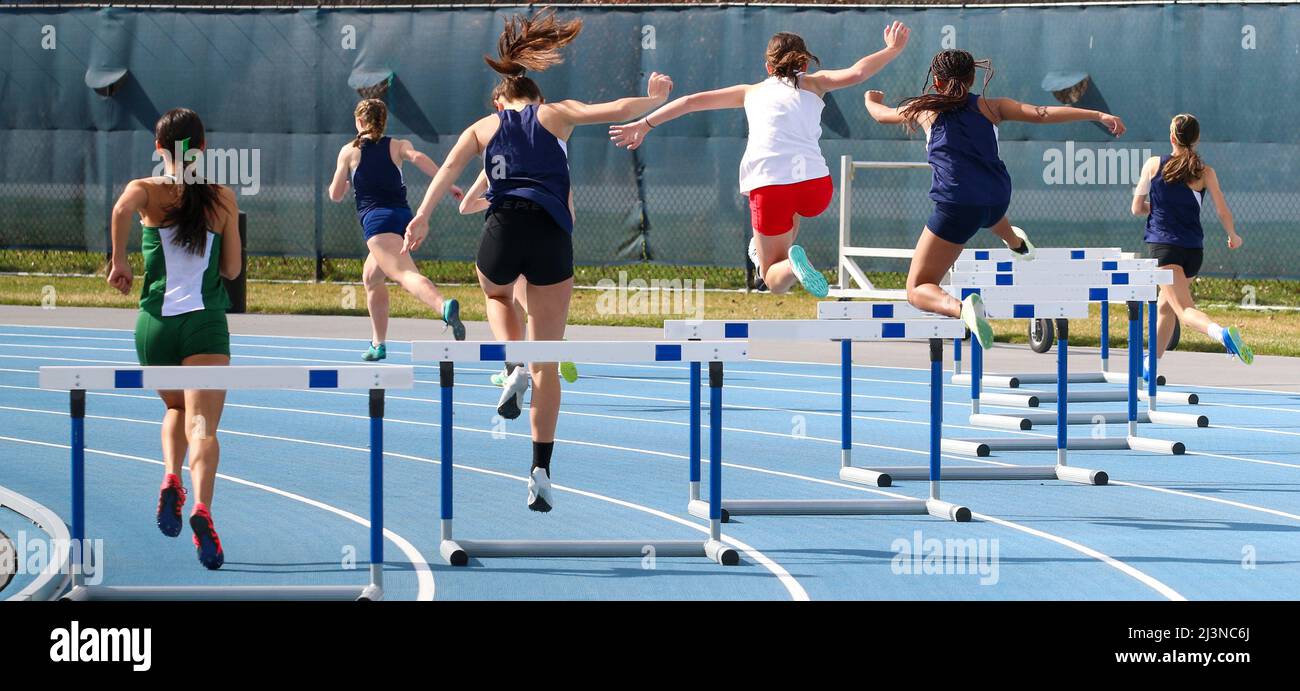 Randals Island, New York, USA - 26. März 2020: Rückansicht von High School Girls, die 400 bei einem Hürdenlauf auf einer blauen Strecke laufen. Stockfoto