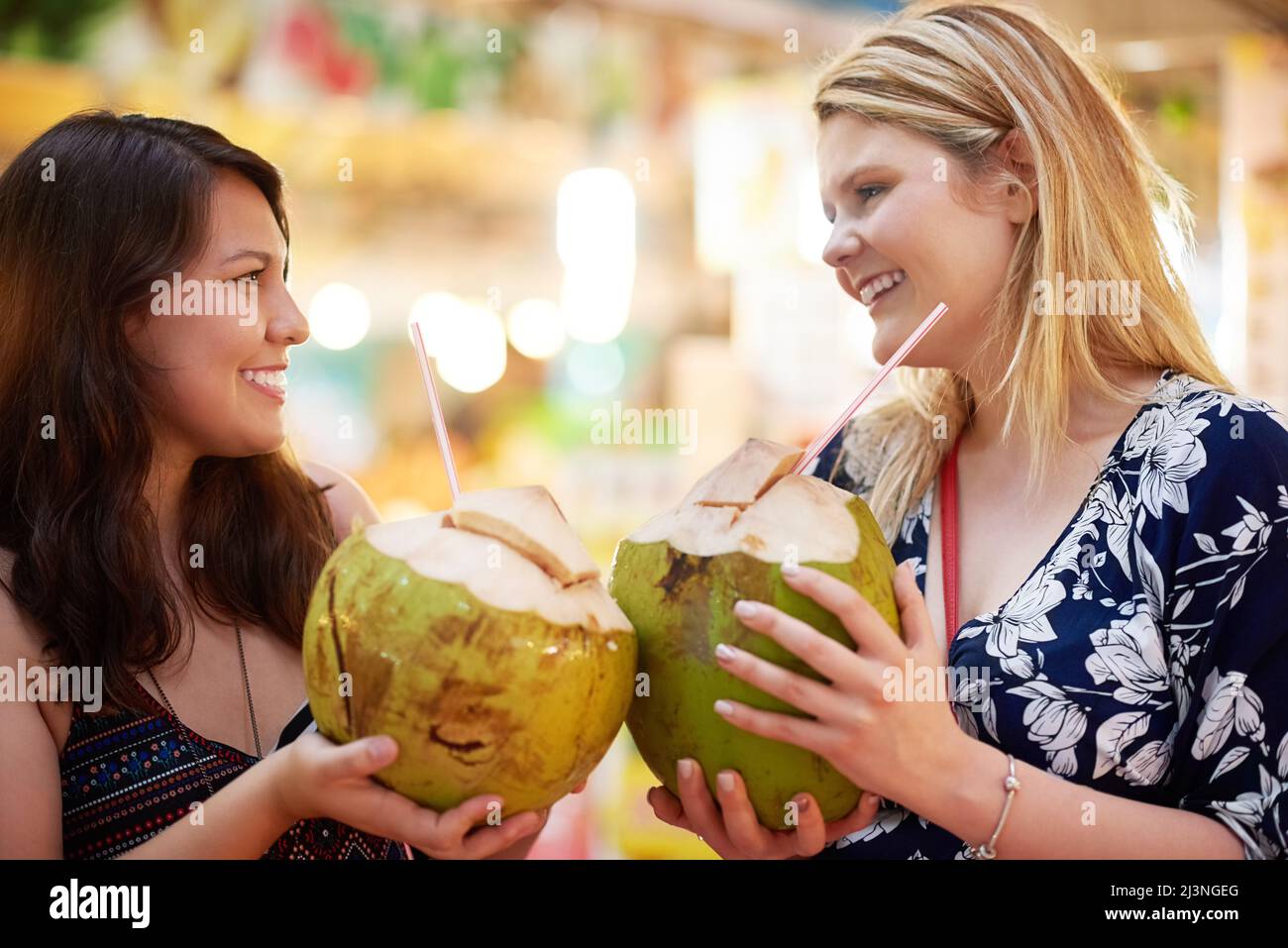 Zusammen auf drei. Kurzer Schuss von zwei jungen Frauen, die in einem ausländischen Lebensmittelgeschäft aus Kokosnüssen trinken. Stockfoto