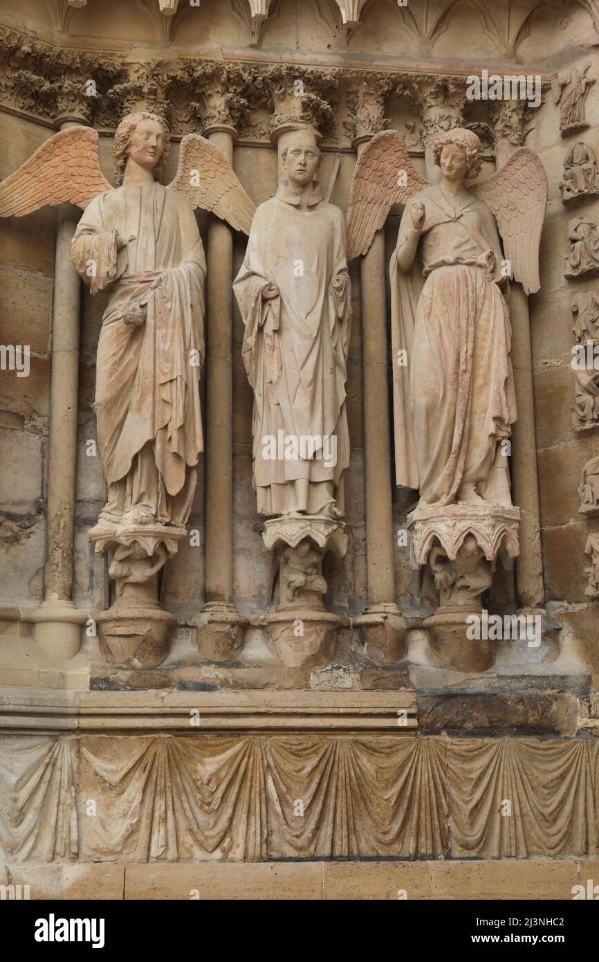 Saint Denis, umgeben von zwei Engeln, die auf dem Nordportal der Westfassade der Kathedrale von Reims (Cathédrale Notre-Dame de Reims) in Reims, Frankreich, abgebildet sind. Die berühmte gotische Statue des lächelnden Engels, die zwischen 1230 und 1245 geschnitzt wurde, ist rechts abgebildet. Die gotische Statue des Saint Denis von Paris wurde zwischen 1220 und 1230 geschnitzt, während die gotische Engelsstatue links nach 1252 geschnitzt wurde. Stockfoto