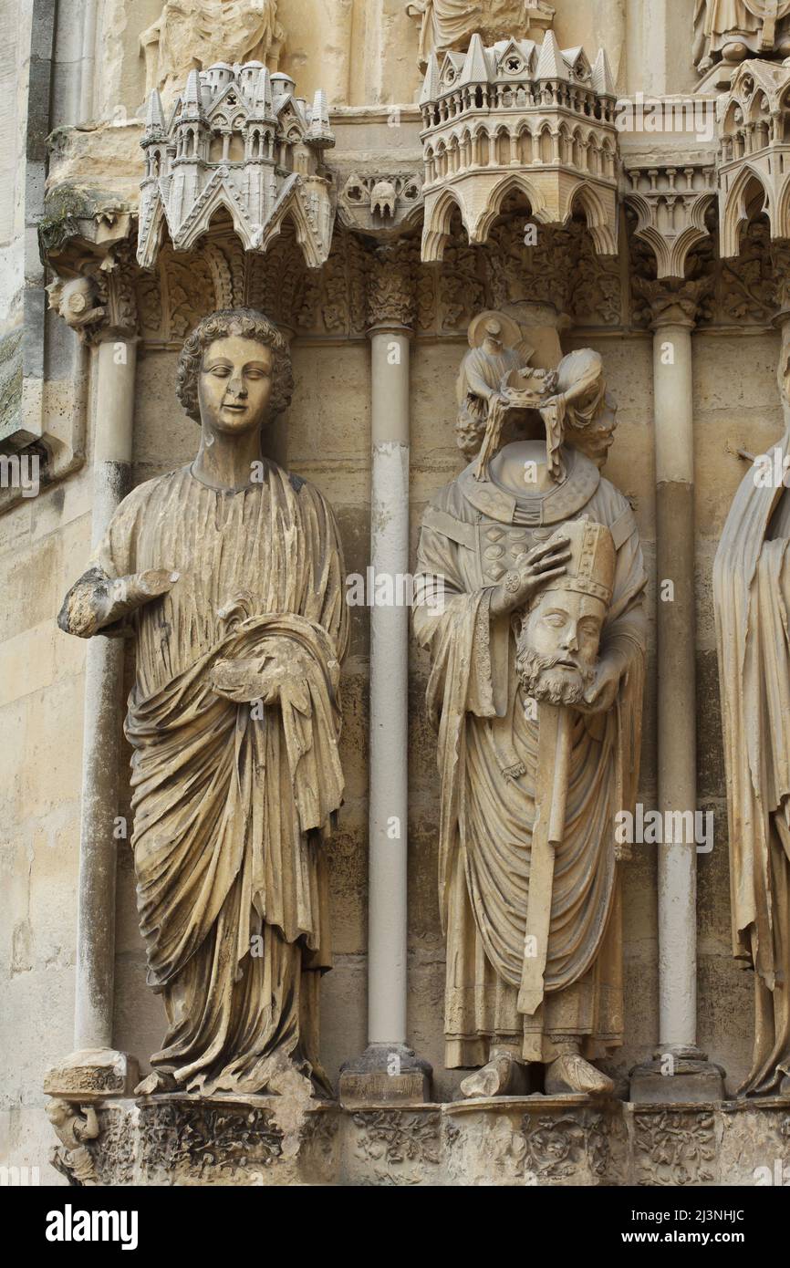 Der Heilige Nicasius von Reims, dargestellt auf dem zentralen Portal der Nordfassade der Kathedrale von Reims (Cathédrale Notre-Dame de Reims) in Reims, Frankreich. Rechts ist der heilige Nicasius abgebildet, links die gotische Engelsstatue. Stockfoto