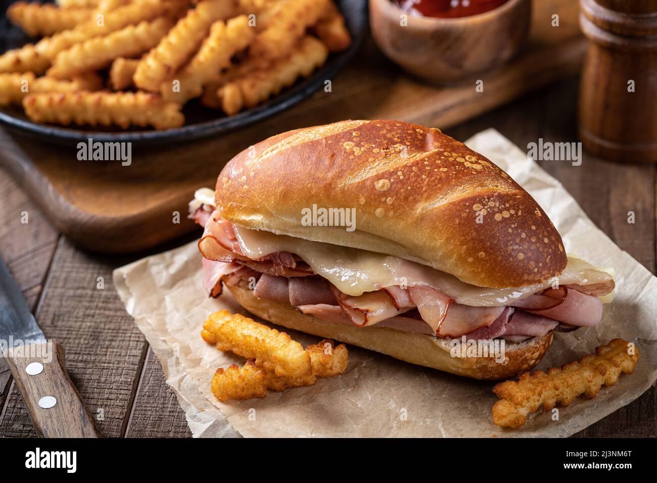Heißer Schinken und Käse-U-Boot-Sandwich mit knusprigen pommes auf einem rustikalen Holztisch Stockfoto