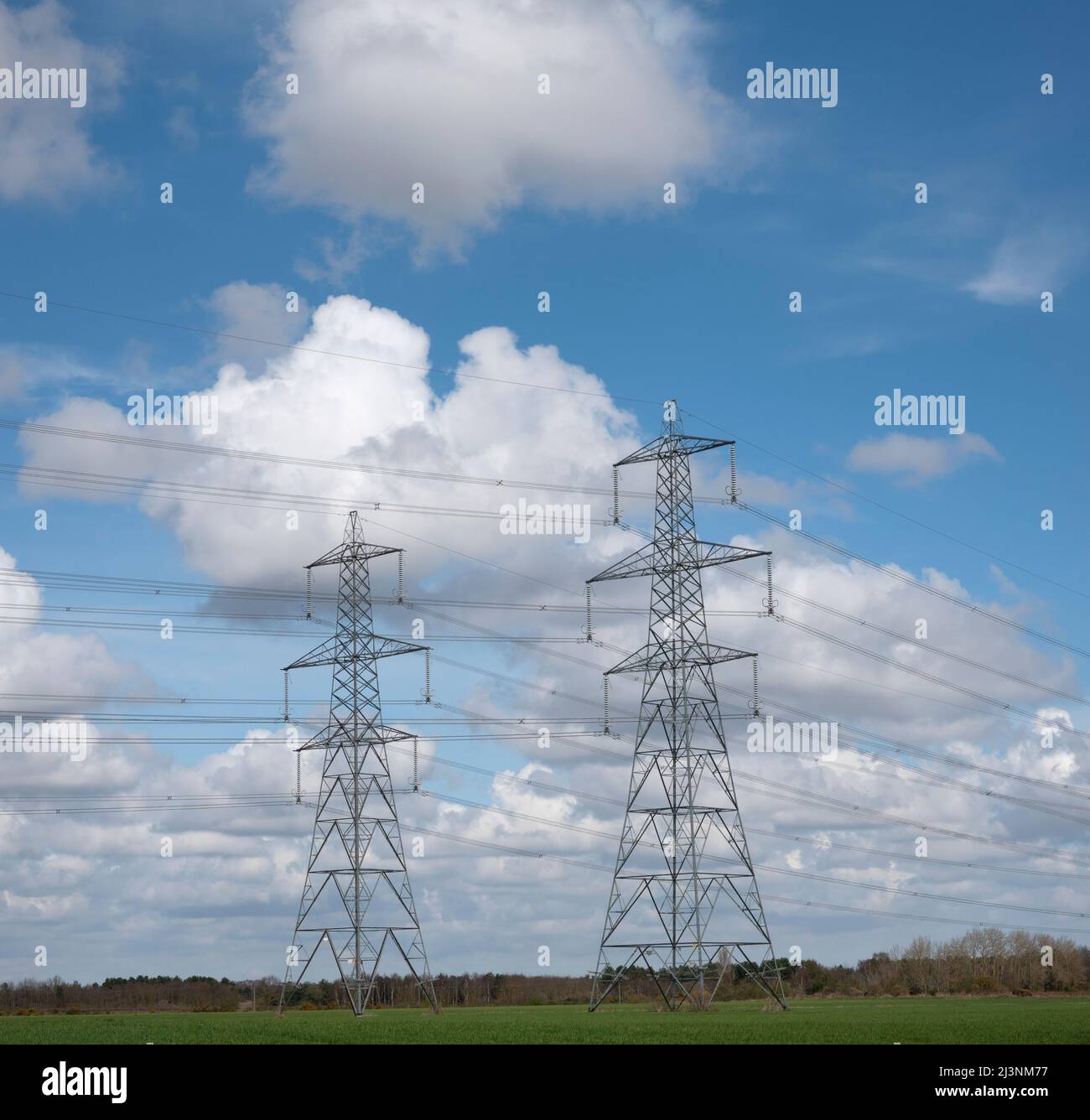 Ein Paar Transmission ragt an einem blauen Himmel mit weißen, flauschigen Wolken dahinter mit einem Hauch von Boden am niedrigen Horizont auf Stockfoto