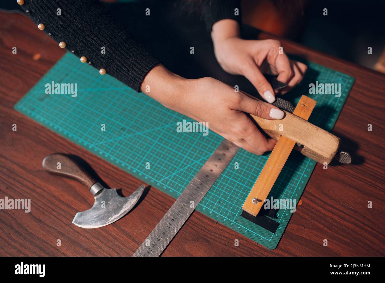 Tanner Frau schneidet Lederwaren in der Werkstatt. Arbeitsprozess des Lederhandwerks. Stockfoto