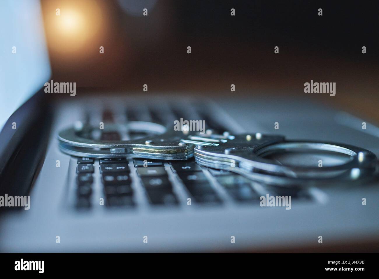 Treffen Sie zusätzliche Vorsichtsmaßnahmen, um sich vor Cyberkriminalität zu schützen. Aufnahme eines Paares Handschellen, die im Dunkeln auf einer Laptop-Tastatur liegen. Stockfoto