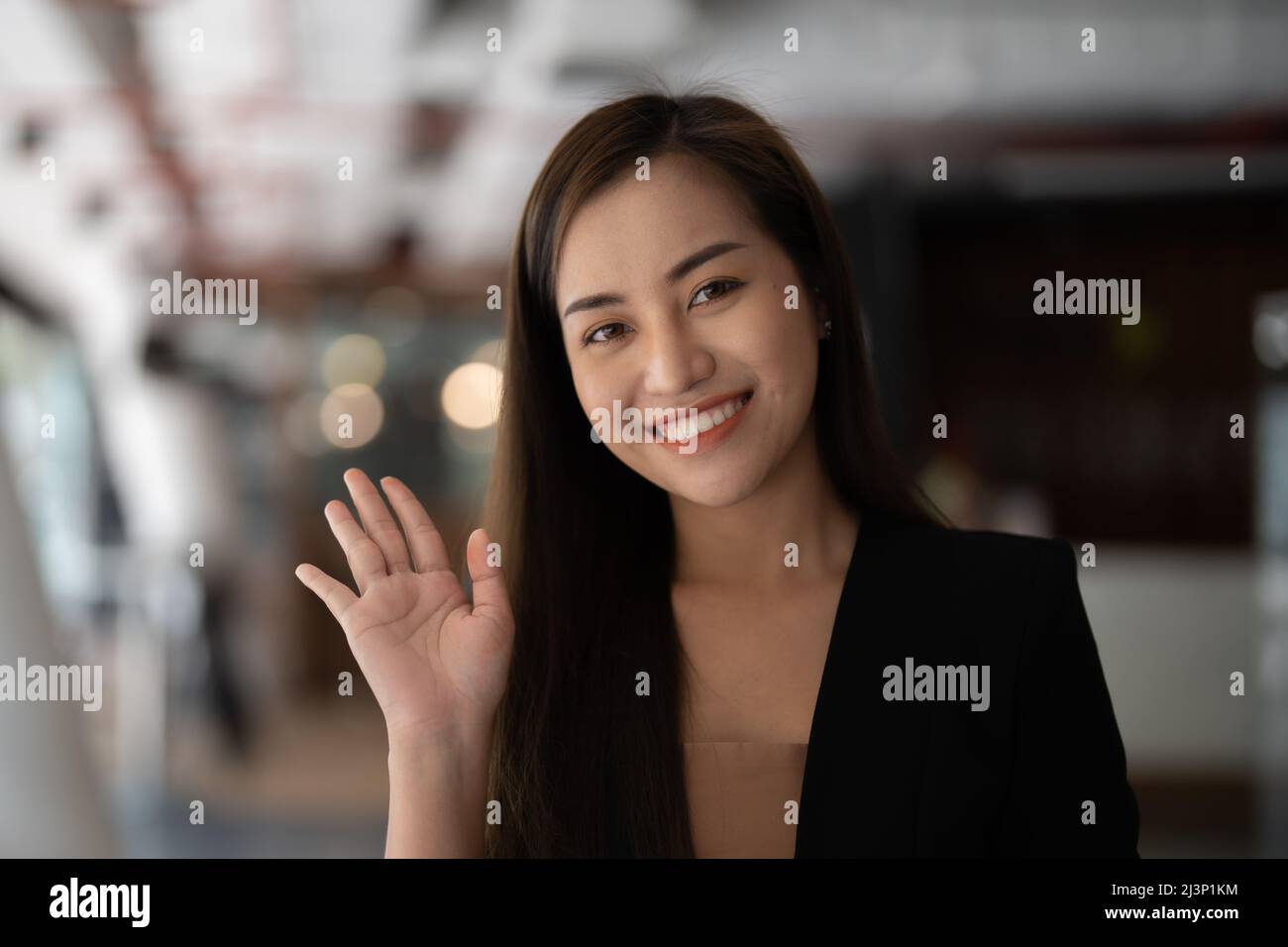 Lächelnde asiatische Frau winkt mit der Hand und schaut auf die Kamera, sie macht einen Videoblog oder ruft zu Hause an, glücklicher, freundlicher Vlogger. Stockfoto