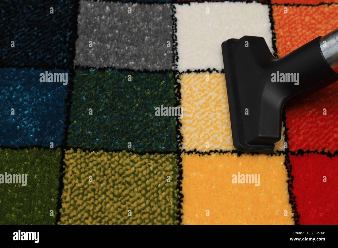 Saugen eines weichen Teppichs mit einem Muster aus farbigen Quadraten. Flauschiger Teppich, Innenelement, Bodenbelag wird vakuumgereinigt Stockfoto