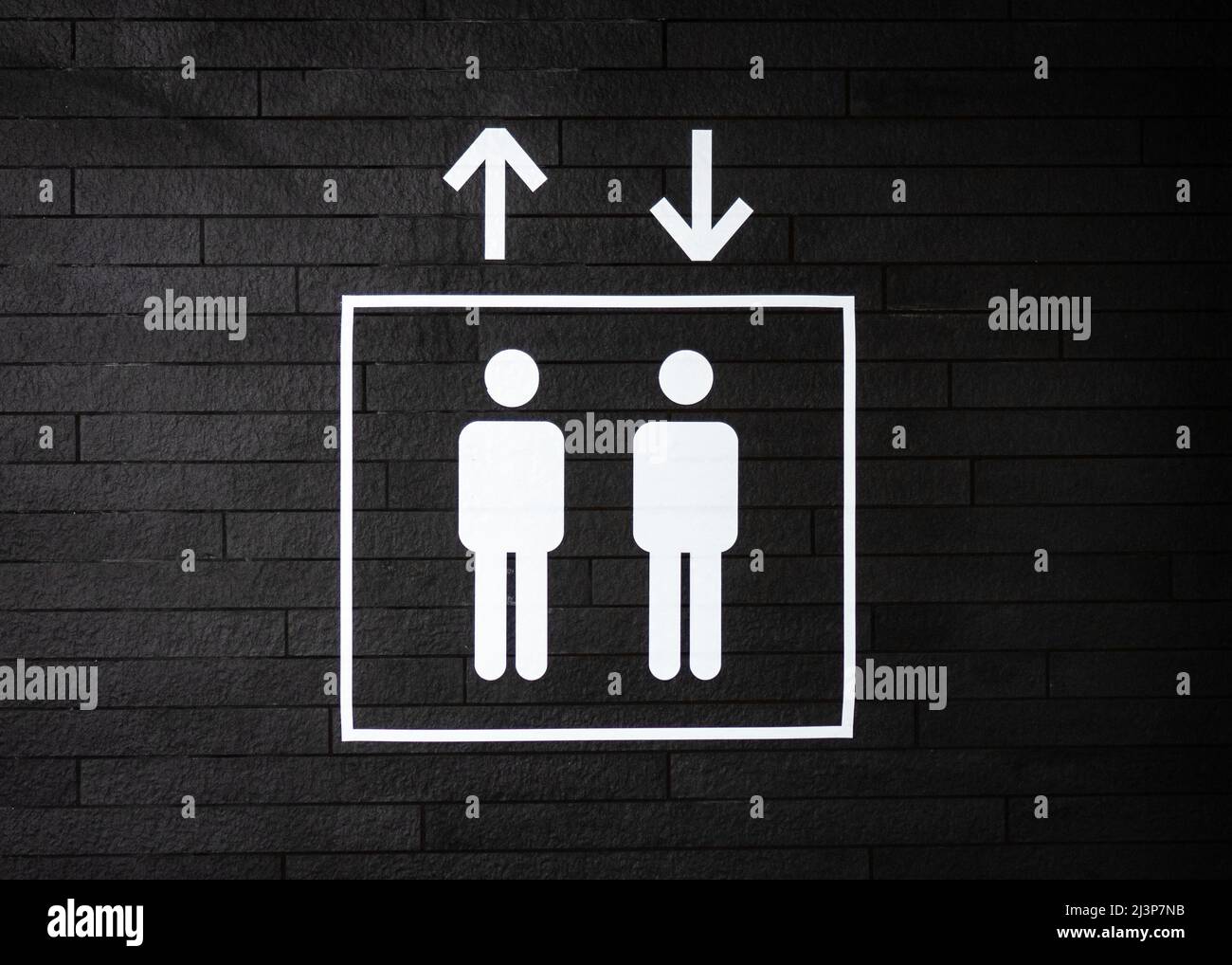 Klare Linien heben Symbol Zeichen gehen auf und ab in weißer Farbe auf dunkelschwarz strukturierte Wand. Zwei Symbole von Männern, die im Aufzug stehen. Stockfoto