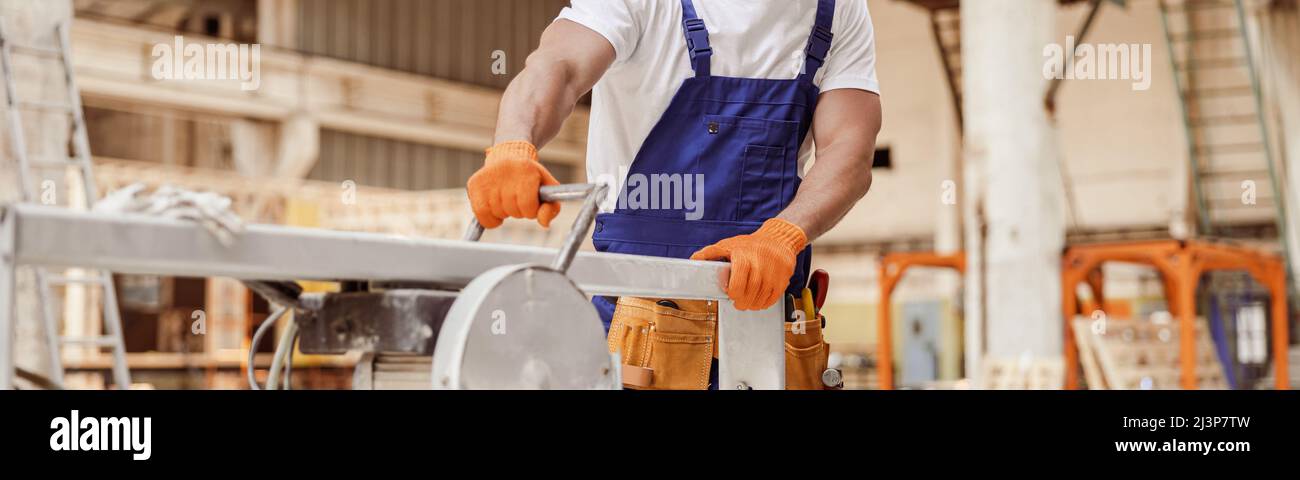 Fröhlicher männlicher Arbeiter mit Sägemaschine in der Werkstatt Stockfoto