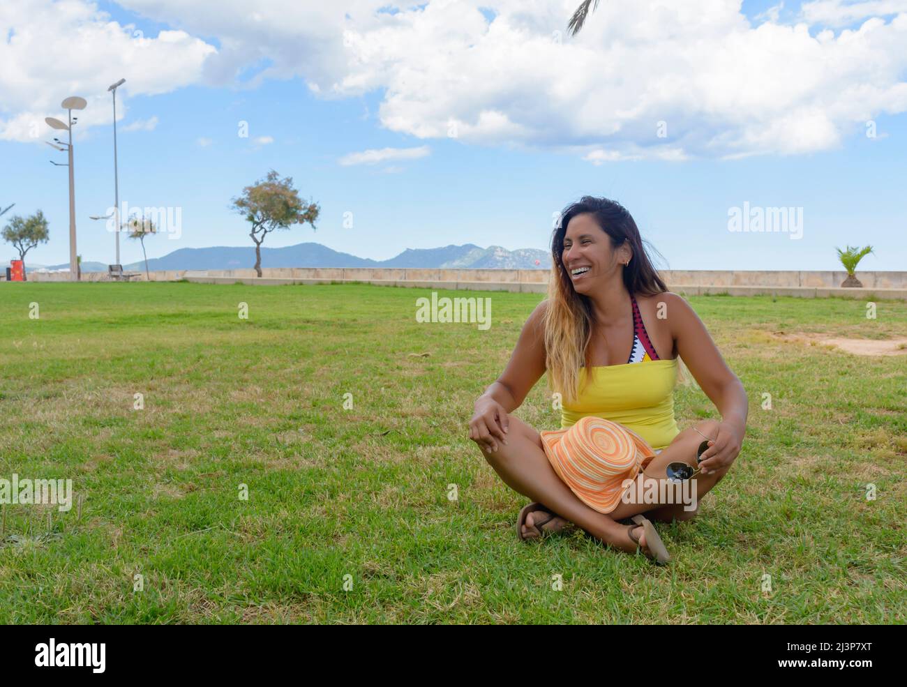 Schöne lateinische Frau 40 Jahre alt, lächelnd sitzt auf dem Rasen eines Parks auf Mallorca, balearen, hollidays Konzept Stockfoto