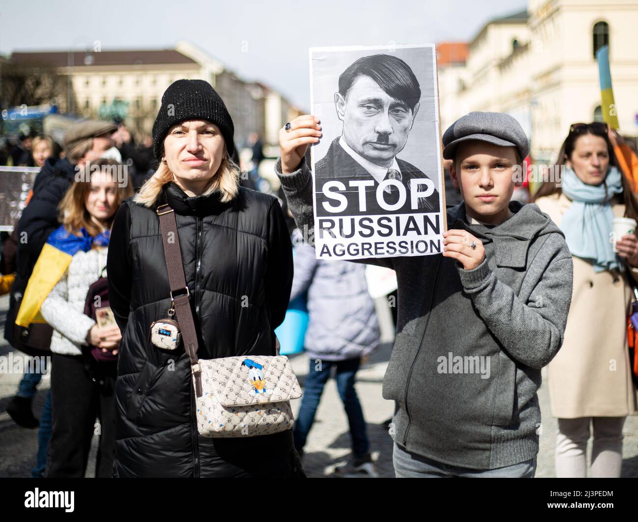 München, Deutschland. 09. April 2022. Junge mit Schild, das Putin zeigt, als Hitler liest: „ Stoppt die Aggression Russlands“. Am 9. April versammelten sich 2022 Menschen in München, Deutschland, um gegen die russische Invasion in der Ukraine zu protestieren und sich an die Toten des Massakers von Bucha zu erinnern. (Foto: Alexander Pohl/Sipa USA) Quelle: SIPA USA/Alamy Live News Stockfoto
