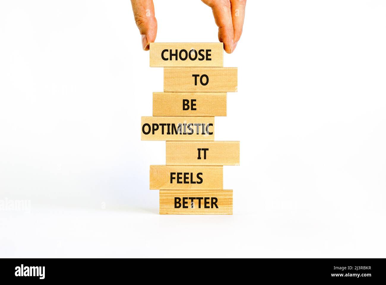 Optimistisch ist das bessere Symbol. Holzblöcke mit Worten Wählen Sie optimistisch zu sein, es fühlt sich besser an. Schöner weißer Hintergrund-Kopierbereich. Geschäftsmann Hand Stockfoto
