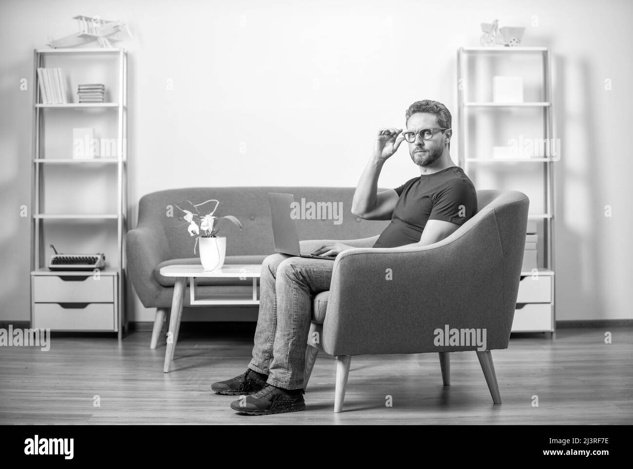 Serious Kerl in roten T-Shirt und Brillen arbeiten am pc im Stuhl, Home Office Stockfoto